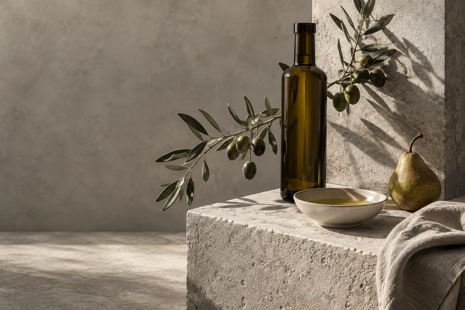 An unlabeled bottle of olive oil, an olive branch and a small bowl of oil on a pale stone block
